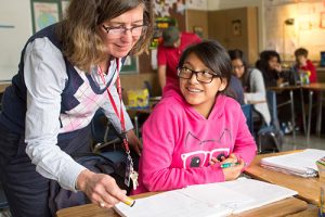 A teacher reviews a student’s work in English class. **THIS IMAGE HAS BEEN DIGITALLY ALTERED TO REMOVE OR OBSCURE STUDENT IDENTITIES.**  Photo by Allison Shelley/The Verbatim Agency for American Education: Images of Teachers and Students in Action