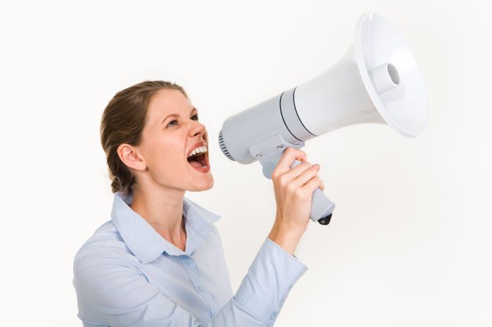 Portrait of businesswoman holding megaphone shouting something on a white background
